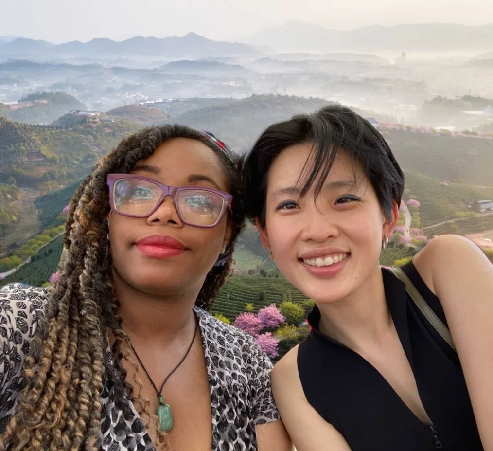 Consuela Hendricks and Angela Lin smile to camera with mountain scenery behind them.