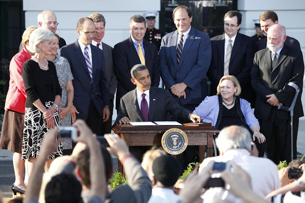 President Obama signs Executive Order on increasing federal employment of individuals with disabilities  during an event commemorating the 20th anniversary of the Americans with Disabilities Act (ADA) on the South Lawn of the White House, July 26, 2010.  (Official White House Photo by Chuck Kennedy). He is surrounded by a group of men and women with light skin tones.