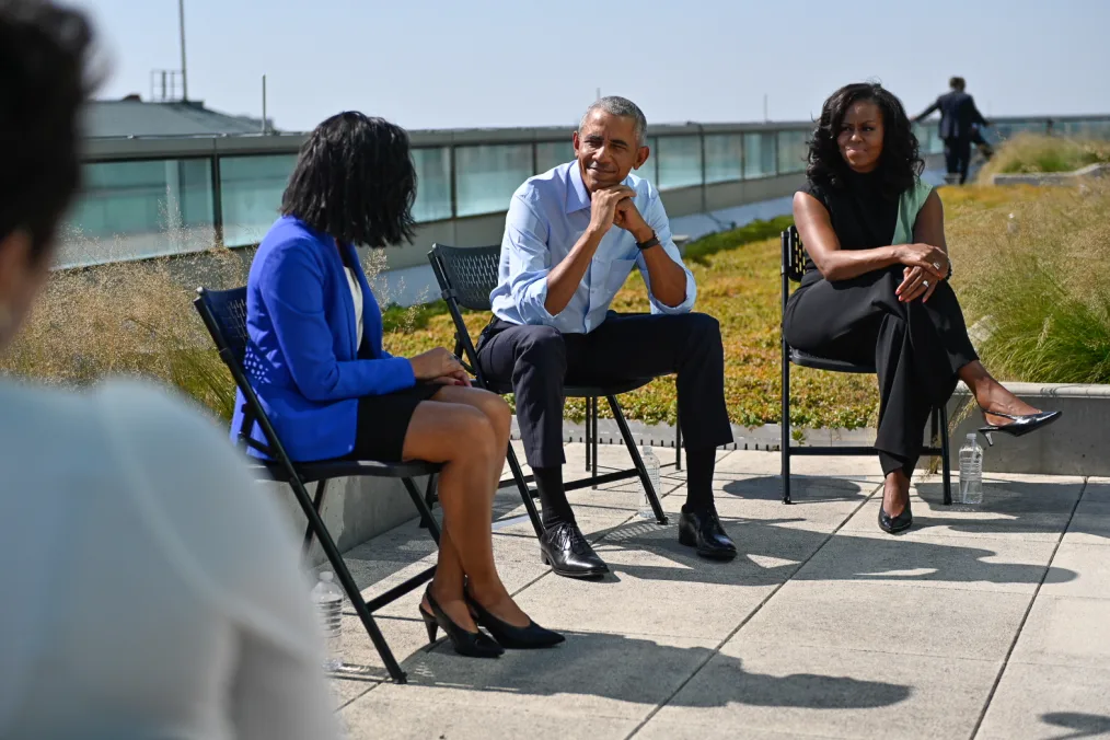 President Obama smiles while speaking with an Obama Foundation Scholar. Mrs. Obama listens to his right.