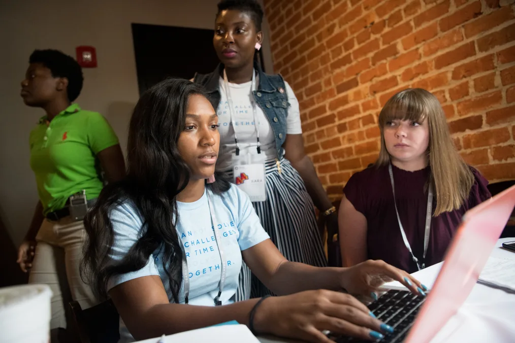 A woman works on a project on a laptop during the CLC Boot Camp, with teammates looking on.