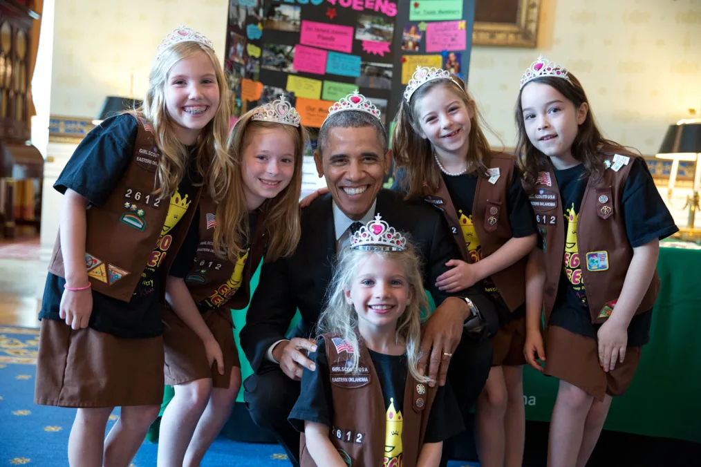 President Obama stands with girls scouts wearing silver and pink tiaras.