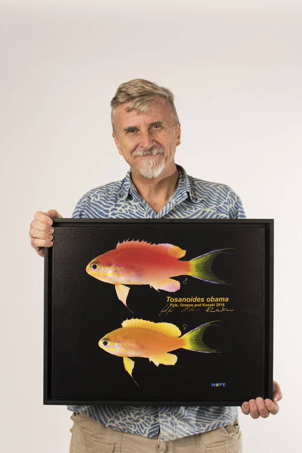 Richard Pyle smiles to camera holding a photograph of the Tosanoides obama fish.