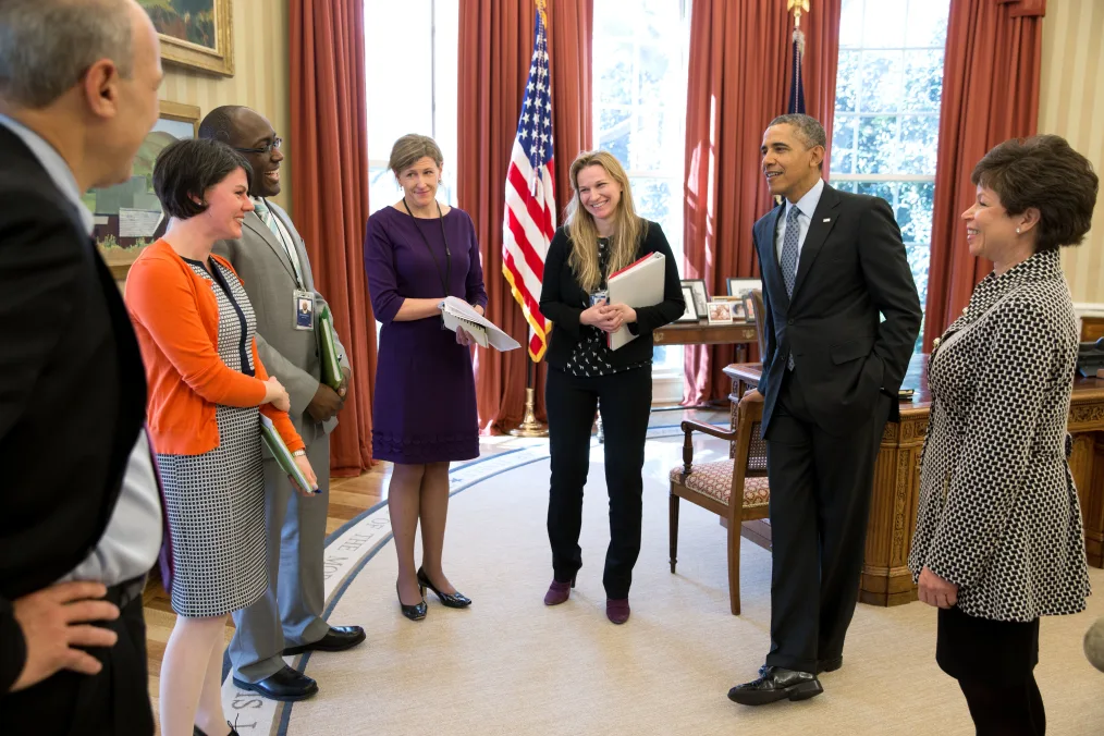 President Barack Obama stands in a circle and receives an update on the Affordable Care Act in the Oval Office. All people in the circle are a range of light to deep skin tones and they are dressed professionally. With the President, from left, are: Phil Schiliro, Consultant; Tara McGuinness, Senior Communications Advisor; Marlon Marshall, Principal Deputy Director of Public Engagement; Jeanne Lambrew, Deputy Assistant to the President for Health Policy; Kristie Canegallo, Advisor to Chief of Staff; and Senior Advisor Valerie Jarrett. 
