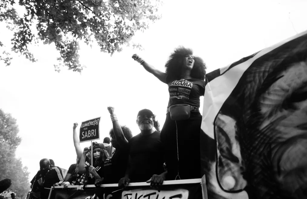 Assa Traoré holds her fist in the air speaking into a megaphone during a protest.