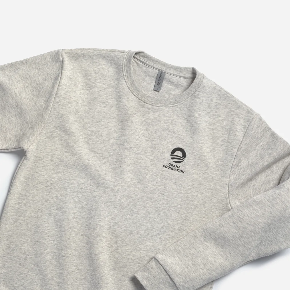 A gray crewneck features The Obama Foundation rising sun logo in black. 