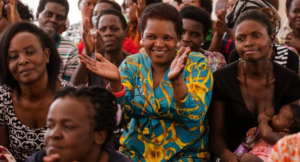 A group of women clap and smile listening to a speaker. One woman