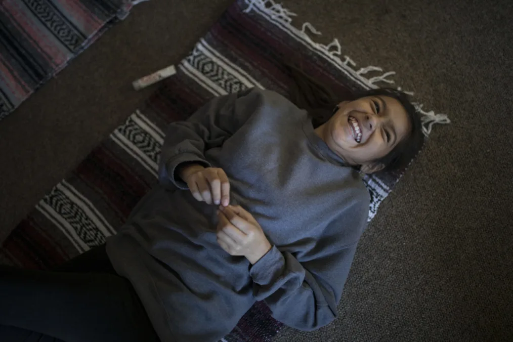 A child with a medium light skin tone laughing on the floor
