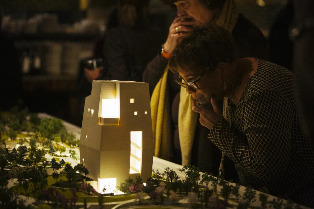 A woman peers into a lit model of the Obama Presidential Center with her arm on her chin.
