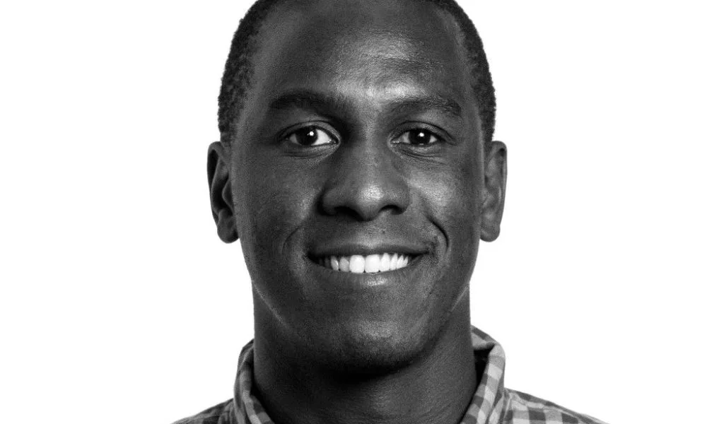 A black man is pictured in black and white wearing a collared shirt.