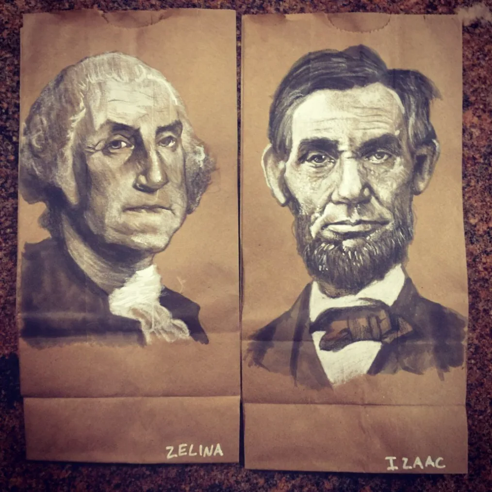 A painting on a brown paper bag of George Washington, a man with a light skin tone and white hair lay besides a painting on a brown bag of Abraham Lincoln, a man with a light skin tone and black hair. The artists names are underneath 
