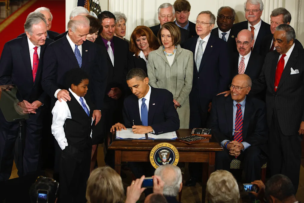 President Barack Obama with Vice President Joe Biden, Members of Congress and special guests, signs H.R. 3590- Patient Protection and Affordable Care Act (health care insurance reform bill) in the East Room of the White House, March 23, 2010. Participants include: Vicki Kenndy, Connie Anderson, Ryan Smith, Mareclas Owens, Health and Human Services Secretary Kathleen Sebelius, Sen. Harry Reid, D-Nev., Sen. Richard Durbin, D-Ill., Sen. Max Baucus, D-Mont., Sen. Tom Harkin, D-Iowa, Sen. Christopher Dodd, D- Conn., House Speaker Nancy Pelosi, D-Calif., Rep. James Clyburn, D-S.C., Rep. George Miller, D-Calif., Rep. Henry Waxman, D-Calif., Rep. Sander Levin, D-Mich., Rep. John Dingell, D-Mich. (Official White House Photo by Chuck Kennedy)
