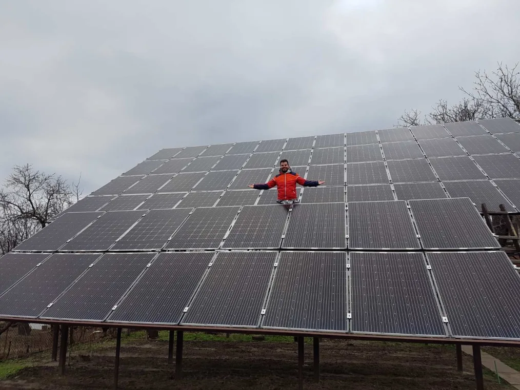 Filip Koprčina, a man with a light skin tone and dark brown hair, stands inside a solar panel grid. He is smiling and wearing a red windbreaker jacket.