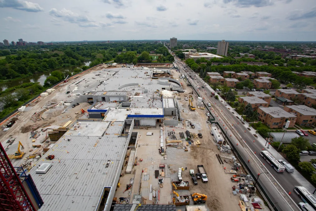 An aerial view of the Obama Presidential Center. Construction tools, cranes, and trucks are seen in the image. Trees and the surrounding community are in the background. 
