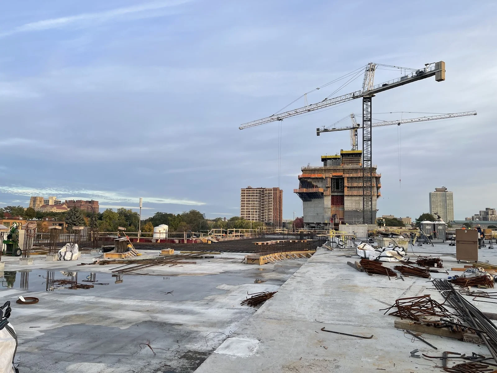 A view of the Museum Building rising to the sky on the site of the Obama Presidential Center. Cranes are in the sky as work continues on the garage rooftop. Construction equipment is scattered throughout.