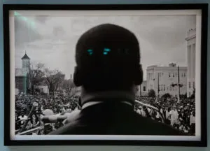 A black and white close up photo of the back of Martin Luther king Jr head with a crowd of people facing him 