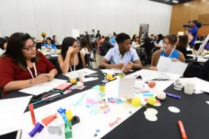 A picture of a diverse group of people sitting at a table with arts and craft materials on the table