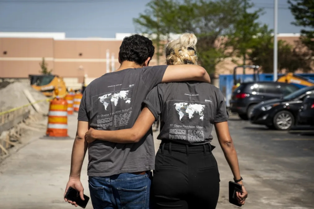 A young woman and man are photographed from behind with their arms around each other in a display of friendship.