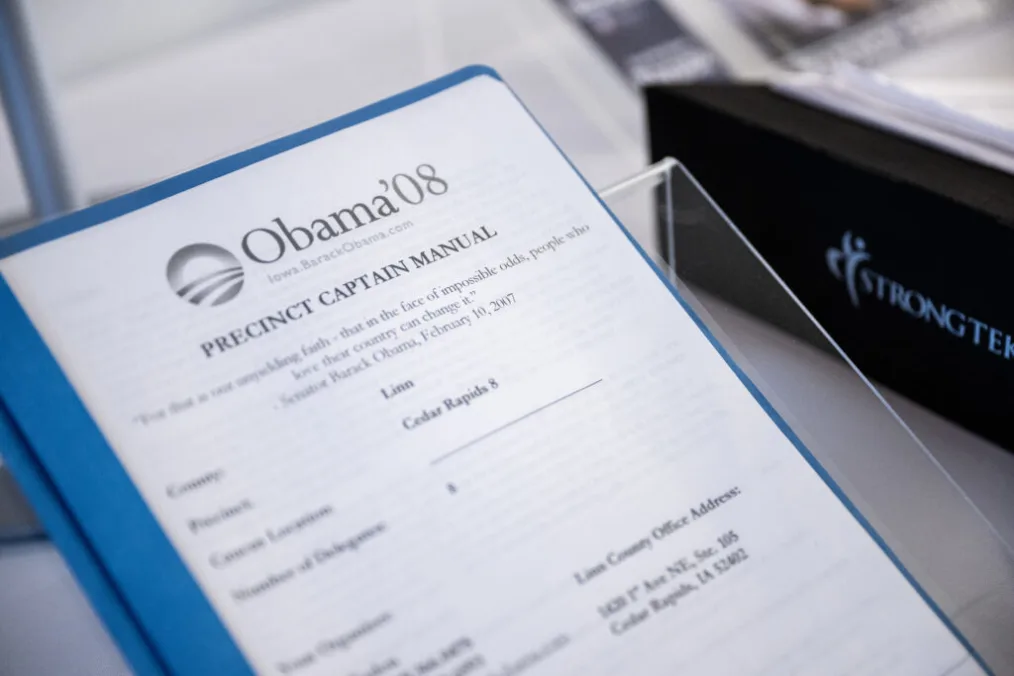 A sheet of paper bound in a clear binder with a light blue spine contains the Obama 2008 campaign Precinct Captain Manual. The Obama campaign logo is at the top of the page in black and white.