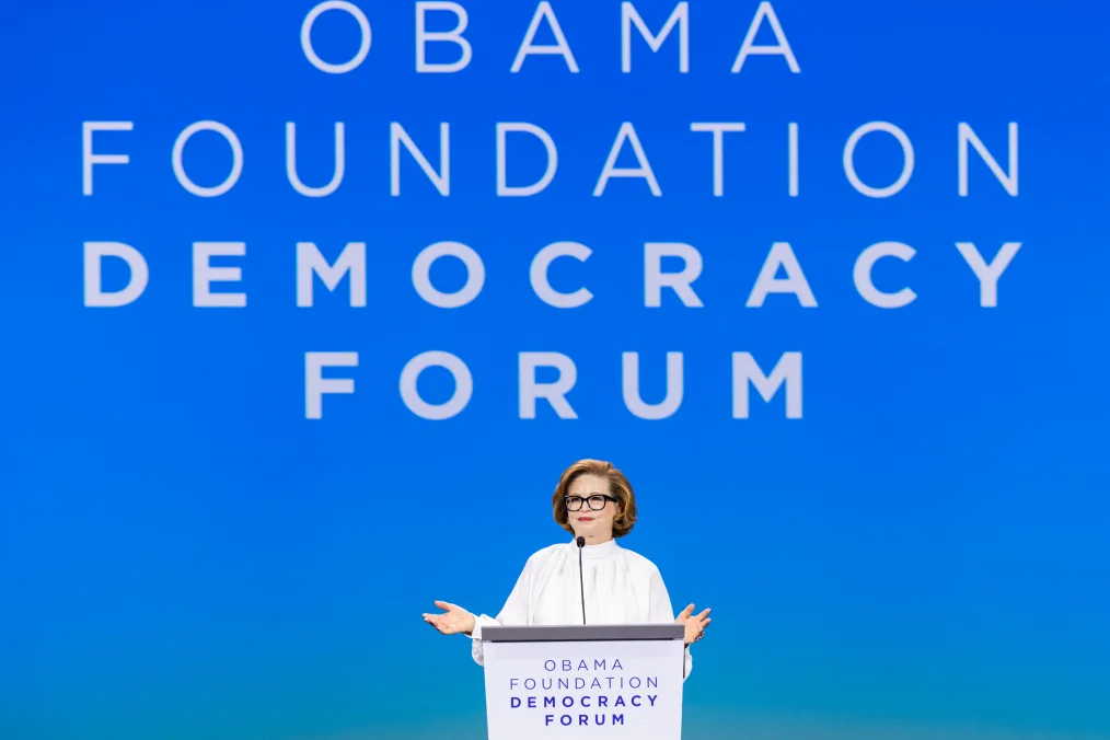Valerie Jarrett, a Black woman with a light skin tone, stands behind a podium as she speaks to an audience. The front of the podium reads, “Obama Foundation Democracy Forum.”