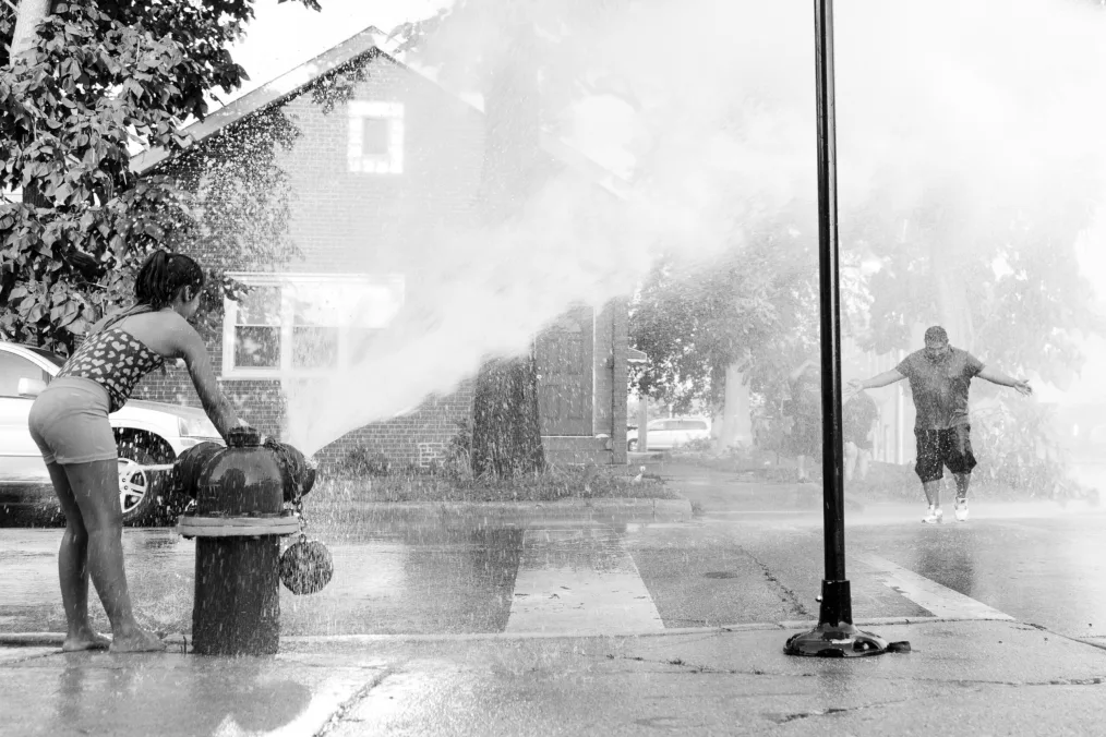 A man stands in the spray of a fire hydrant. 