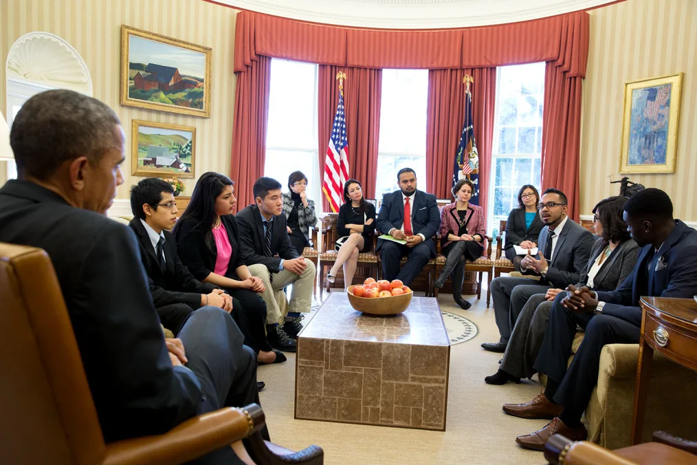 President Obama meets with a group of people with various skin tones in the oval office.