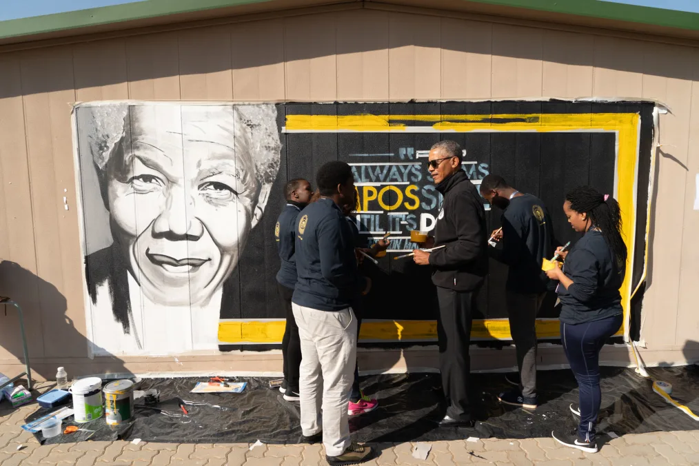 President Obama paints a black, yellow, and white mural with young people of various skin tones.