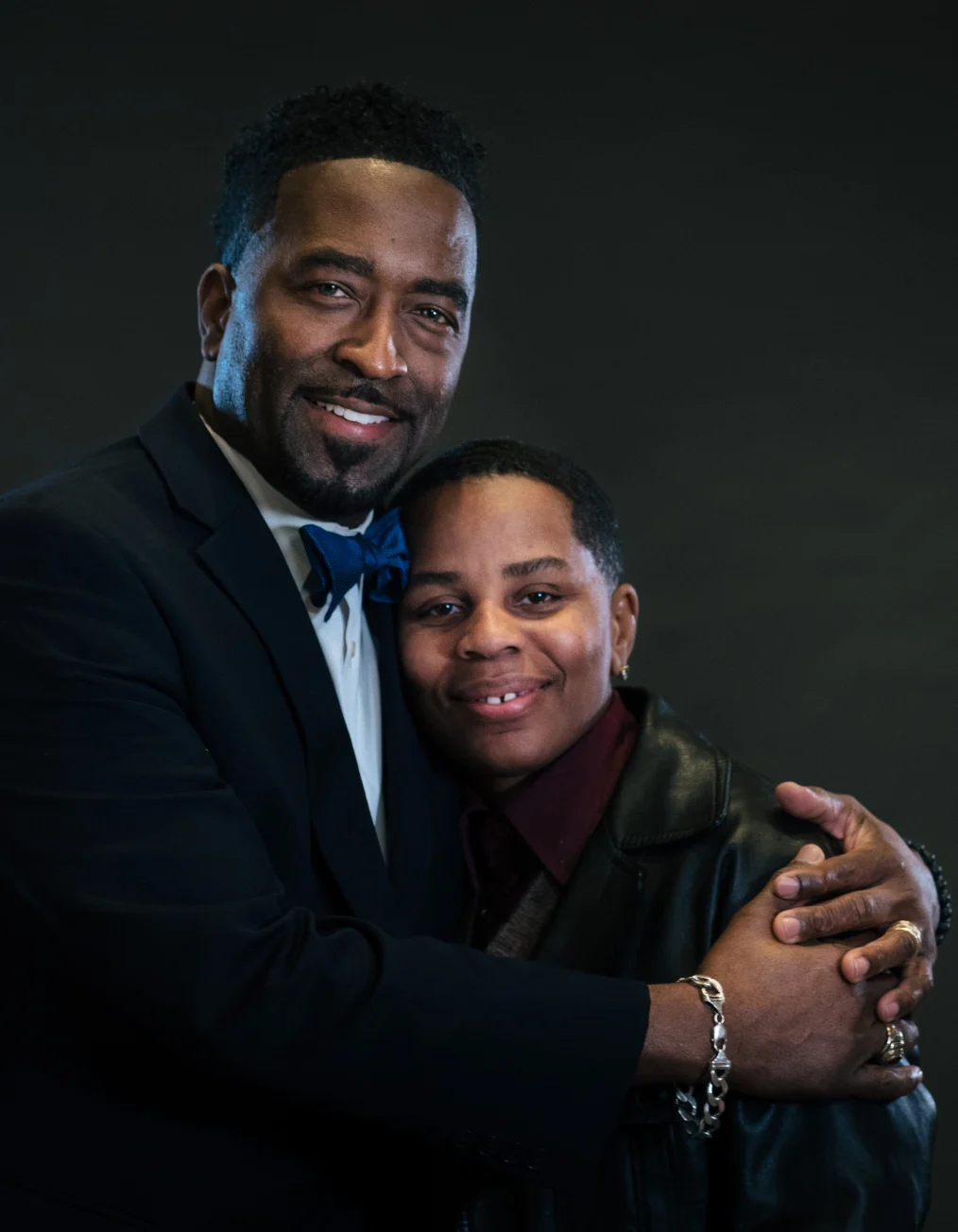 In this picture, two people with deep skin tones are shown smiling toward the camera who wear
business casual and business professional clothes.