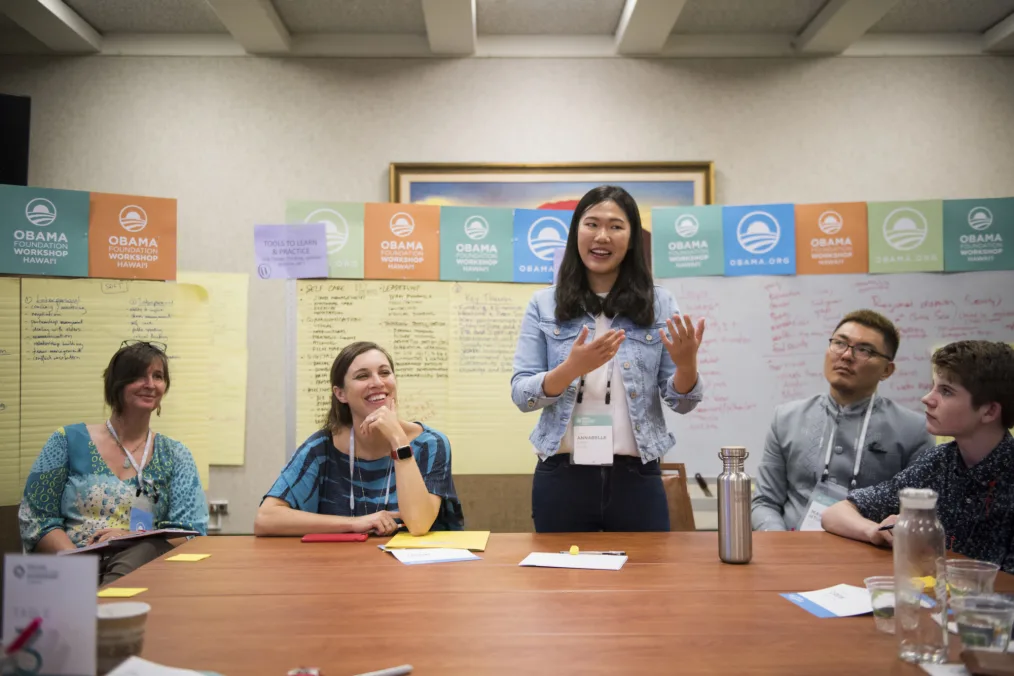 A young woman stands and speaks to a group.