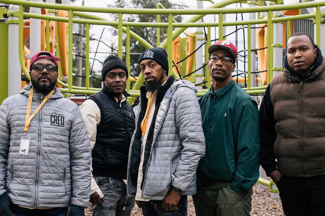 Five men, street outreach staff with Chicago CRED, stand in a playground.