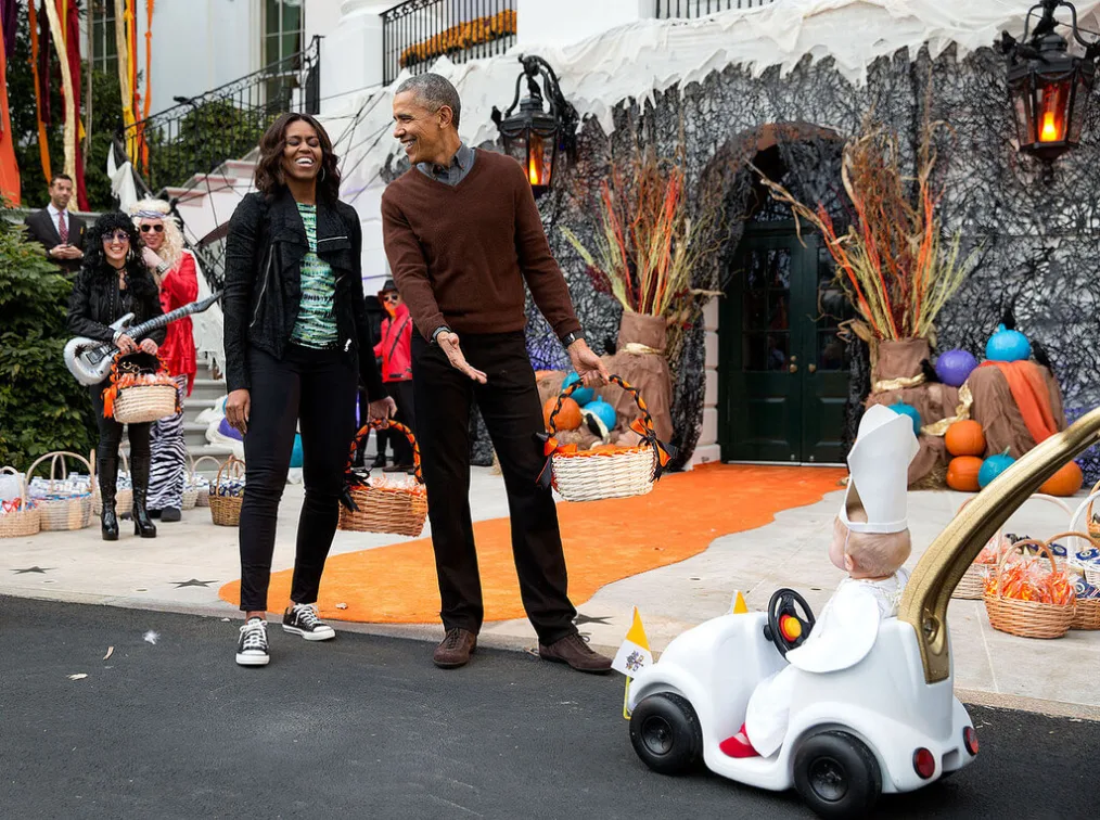 "The President and First Lady react to a child in a costume and mini vehicle a during a Halloween event 