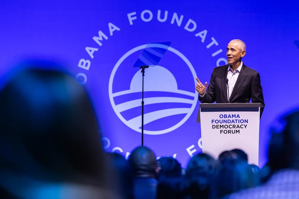 President Obama speaks at the 2024 Democracy Forum. Behind him a sign reads, “Obama Foundation Democracy Forum.” 