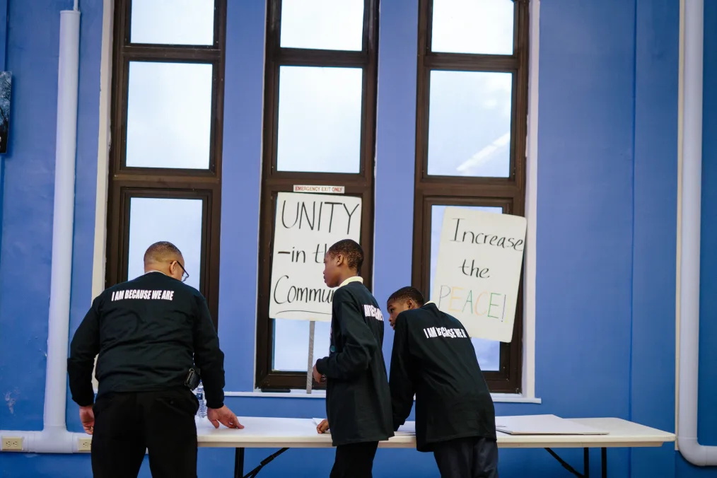 Three Black men with a range of light to deep skin tones create posters at the Black Family Development in Detroit, Michigan. The back of their shirts read, “I am because we are.”