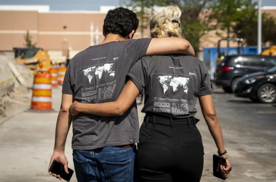 A young woman and man are photographed from behind with their arms around each other in a display of friendship.