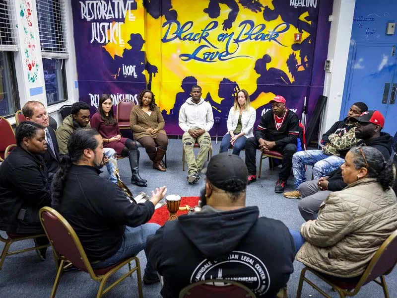 A group of young people sit in a circle in conversation. The wall behind them reads "Black on Black Love."