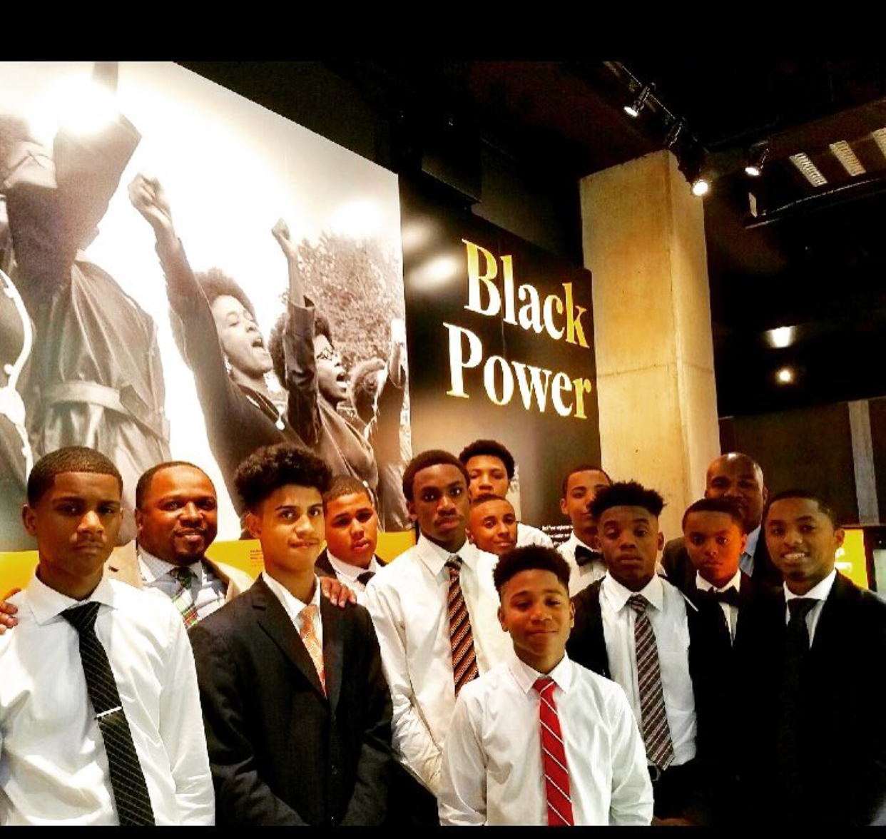 A group of young Black men in suits and ties pose for a photo in front of a large image with the words "Black Power."