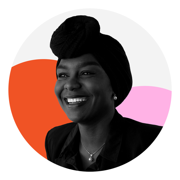 A Black woman is facing the camera smiling with her teeth showing she is wearing a dark head wrap, dark blouse, a pearl necklace and pearl earrings. The photo is black and white and features two circles, one which is orange and the other pink. 
