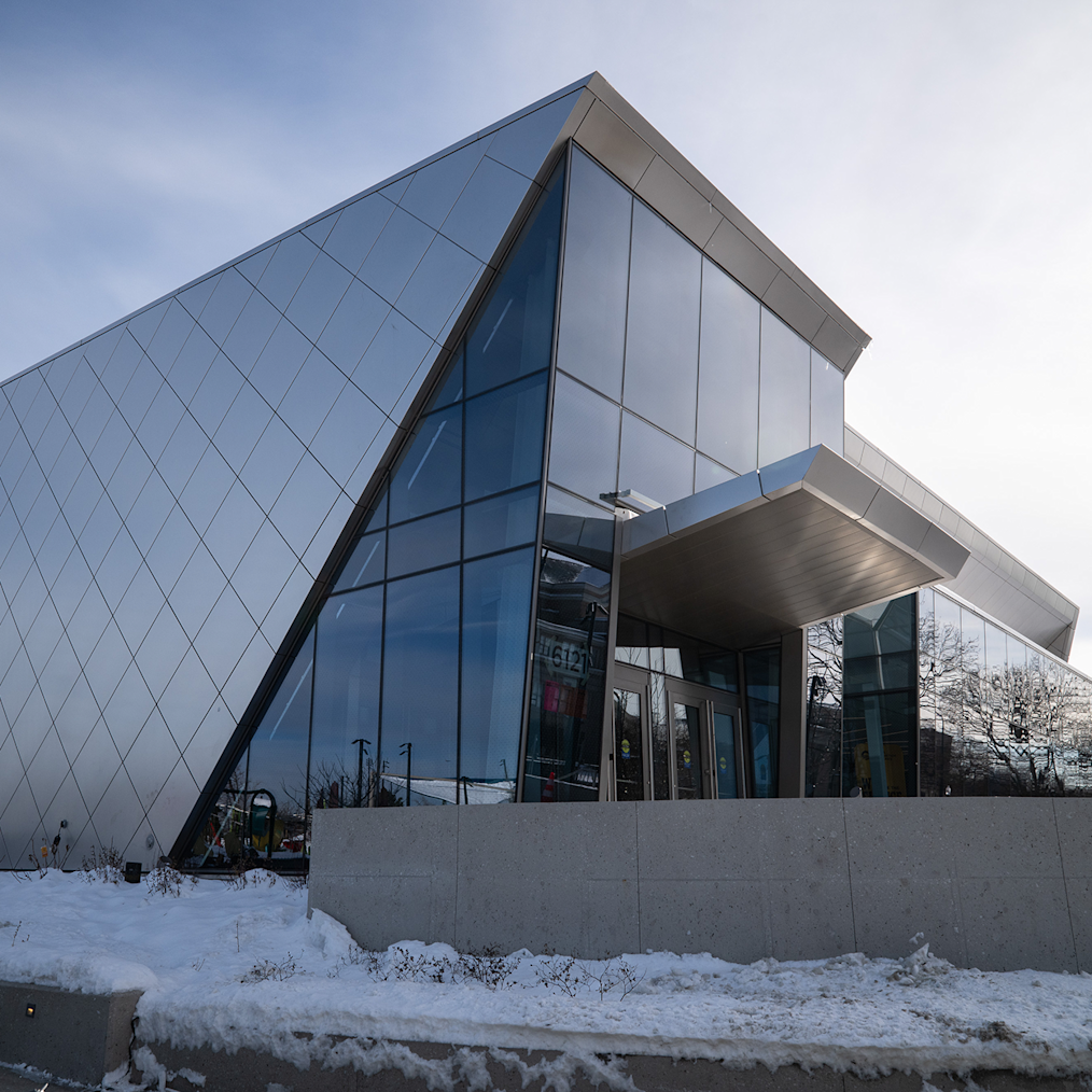 An up close shot of the window panels at the entrance of Home Court at the Obama Presidential Center on a snowy day. The building is gray and metal. 