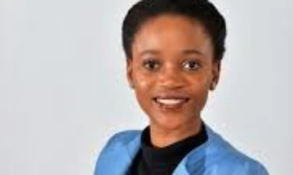 Bogolo J. Kenewendo, a black woman with a medium-deep skin tone and low haircut wearing a black turtleneck and light blue blazer smiles toward the camera.