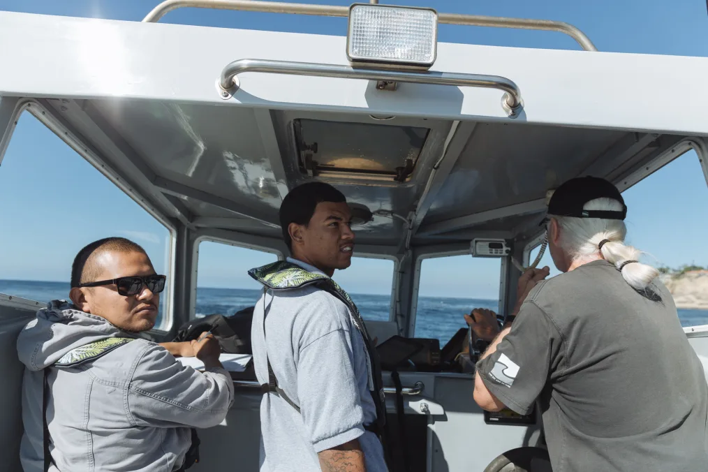 Three men with light skin tones drives a boat on the sea