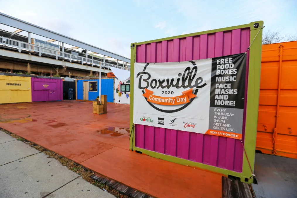 Colorful metal shipping containers. A hot pink one in front has a sign that reads "Boxville 2020 Community Day." 