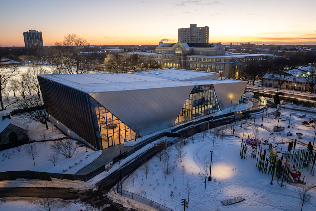 An exterior shot of Home Court at the Obama Presidential Center on a snowy night. Behind Home Court is the Griffin Museum of Science and Industry. 