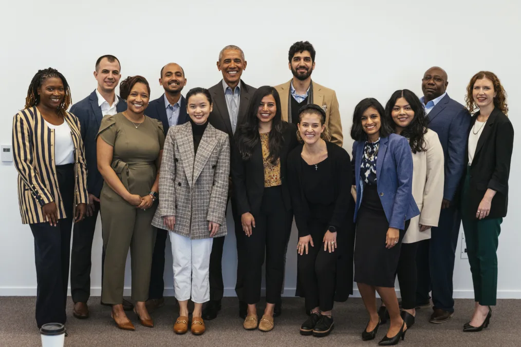 A group of twelve Obama Scholars dressed in business casual attire stand and pose for a group photo with President Obama following roundtable meeting.