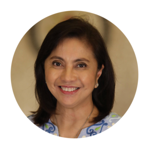 Leni Robredo smiles at the camera. She has medium skin and shoulder length black hair. She is wearing a blue and green patterned top.