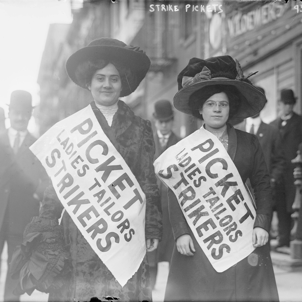 A black and white photo of two well dressed White women wearing a sign that reads, “Picket Ladies Tailors Strikers.” The 
Toward a More Perfect Union is an exhibit featuring artifacts from labor and civil rights movements that explore the ongoing struggle for democratic progress in American history.