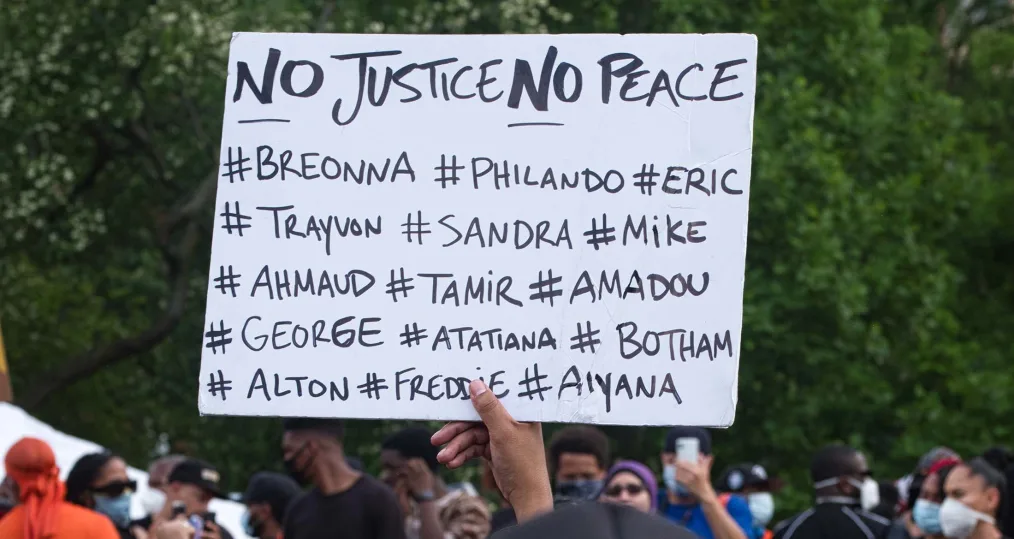 A hand holds up a sign that reads "No Justice. No Peace." alongside hashtags of Black people killed.