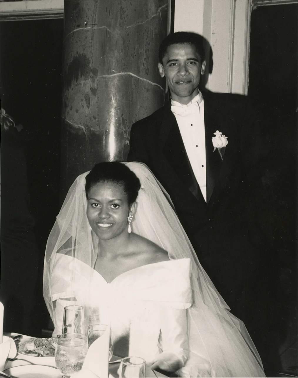 A black and white photo of President and Mrs. Obama on their wedding day, Oct. 3, 1992. President Obama is standing behind a seated Mrs. Obama. 