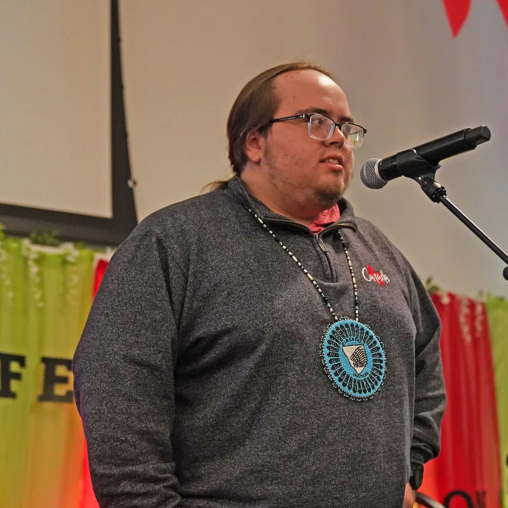 Nick Kennedy, a college-age Native American young man, stands at a microphone while addressing a small crowd.