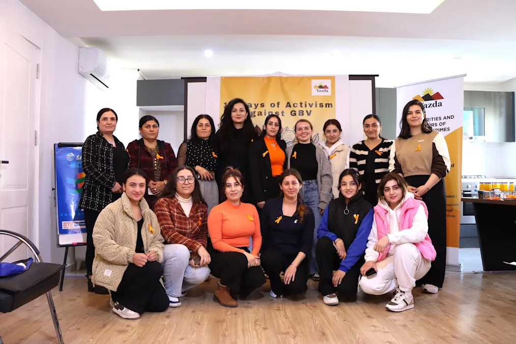 Natia Navrouzov poses with 14 members of Yazda. All are smiling and have light skin tones. 