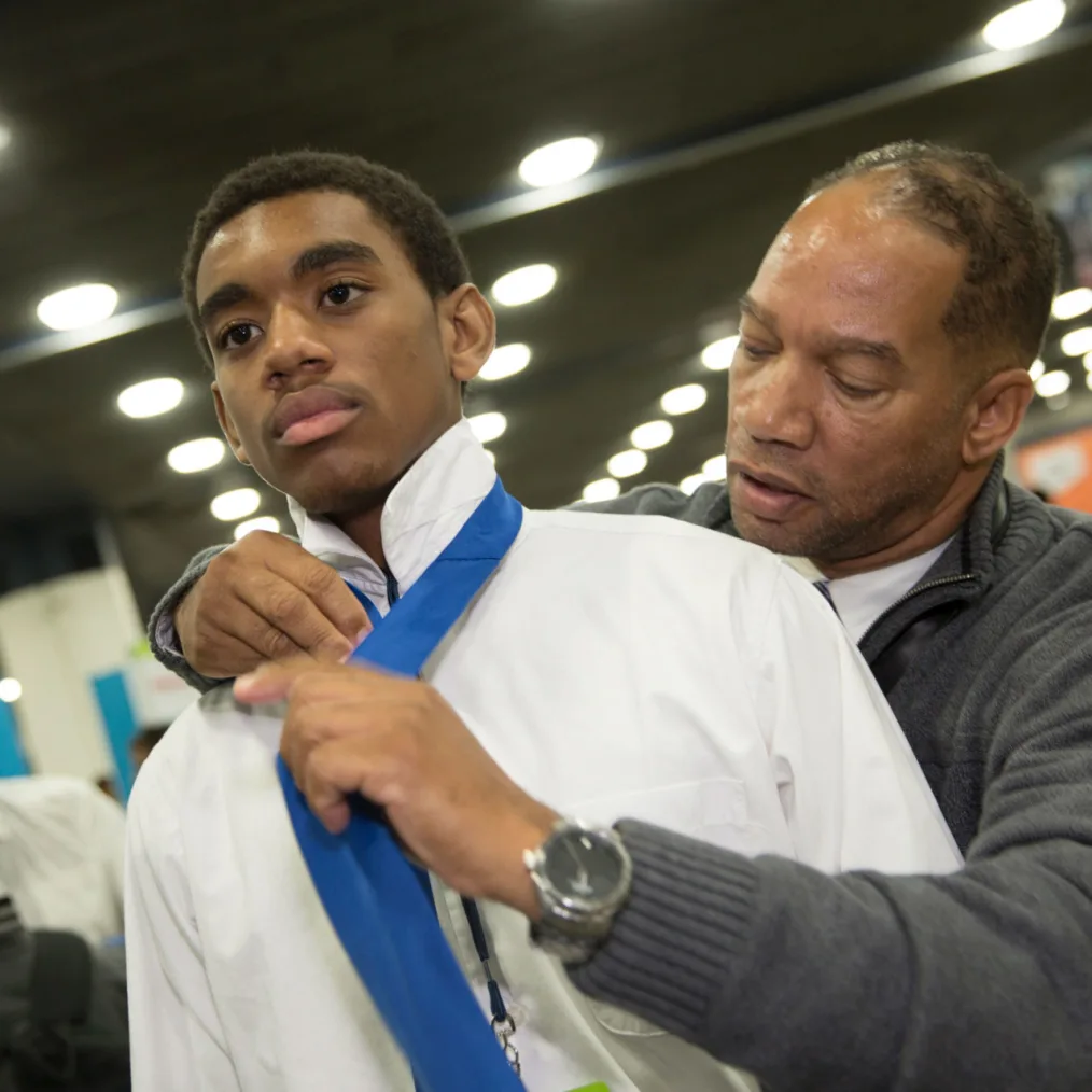 A man with a medium skin tone helps a boy with a medium-deep skin tone put on a tie