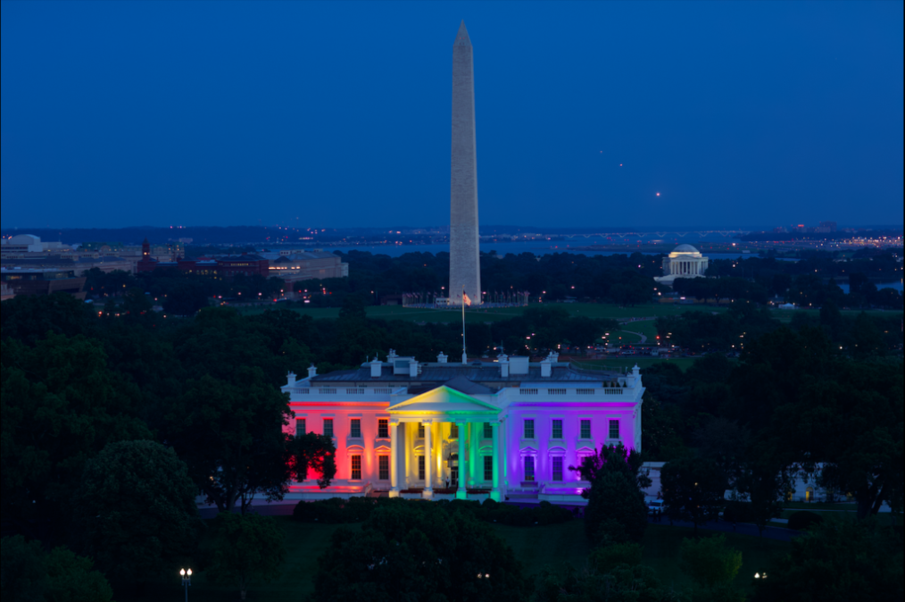 The White House lit in rainbow colors with the Washington Monument in view behind it.